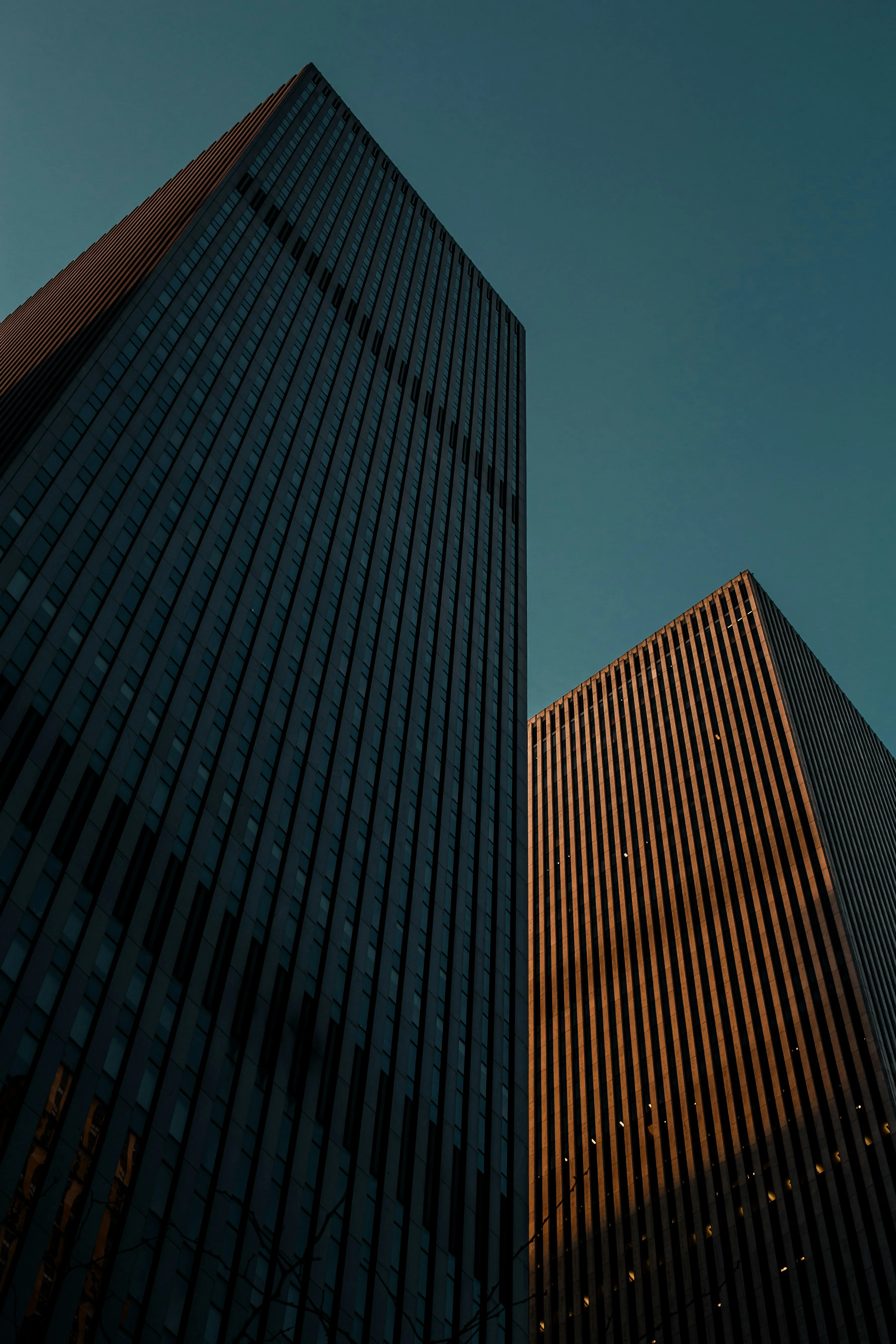 An undershot image of two tall skyscraper buildings against a blue sky.