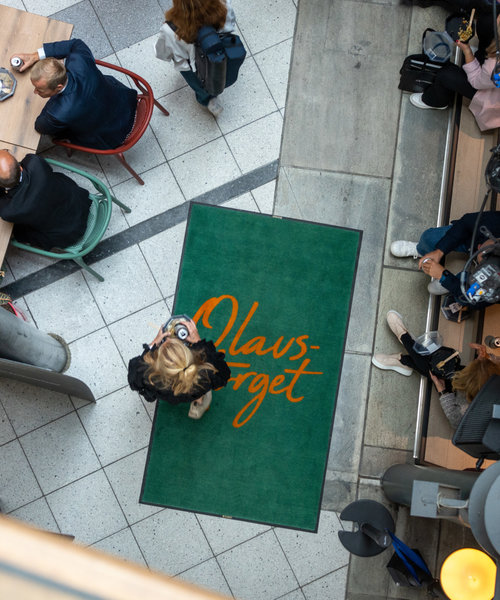 A woman walks across a door mat saying Olavstorget.