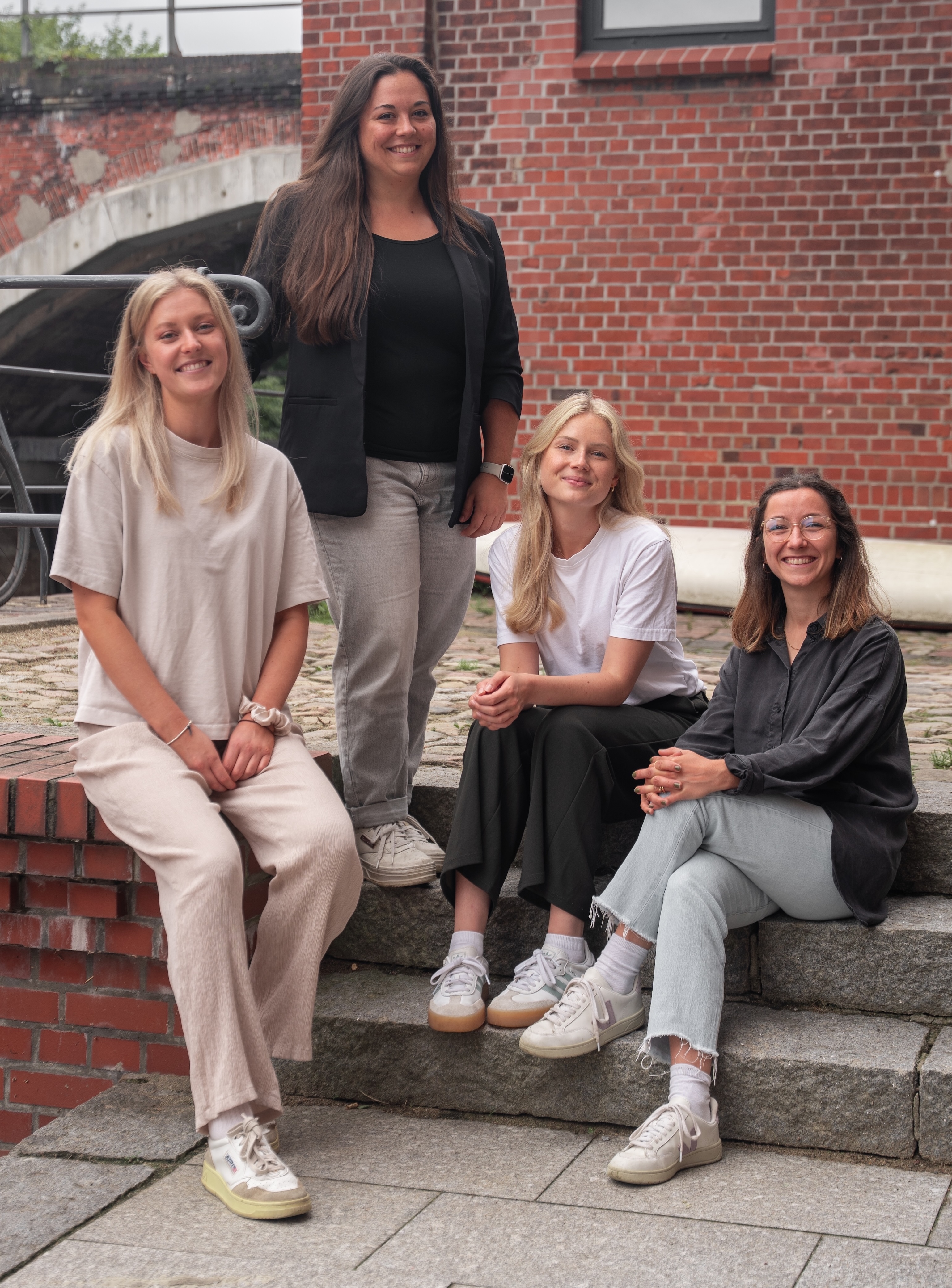 Geschäftsführerinnen Lena Brech und Mitarbeitende sitzen lächelnd auf einer Steintreppe – Vision und USP von moveUPv