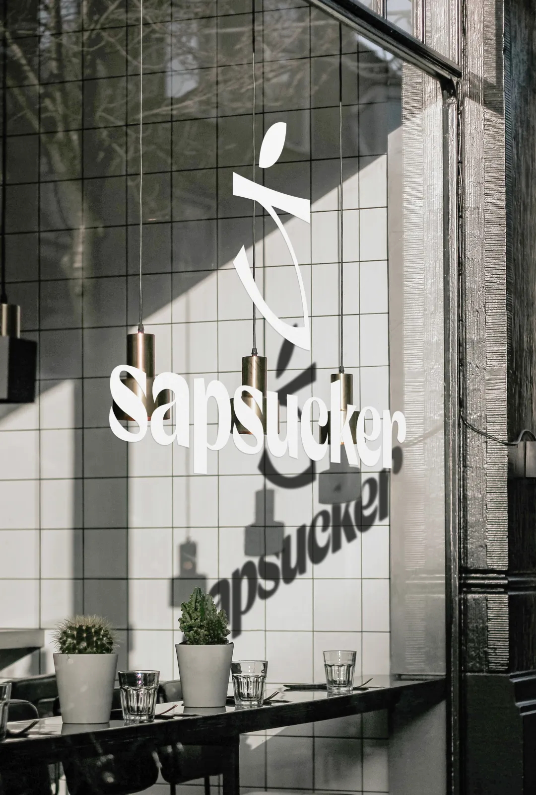 Sapsucker logo applied as a white decal on a café window, with its reflection visible inside.