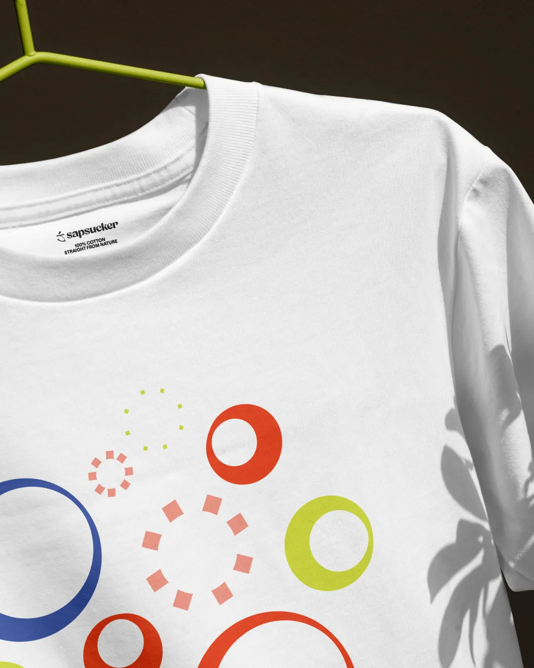 White T-shirt with colorful abstract bubble shapes and the Sapsucker logo printed on the collar tag.