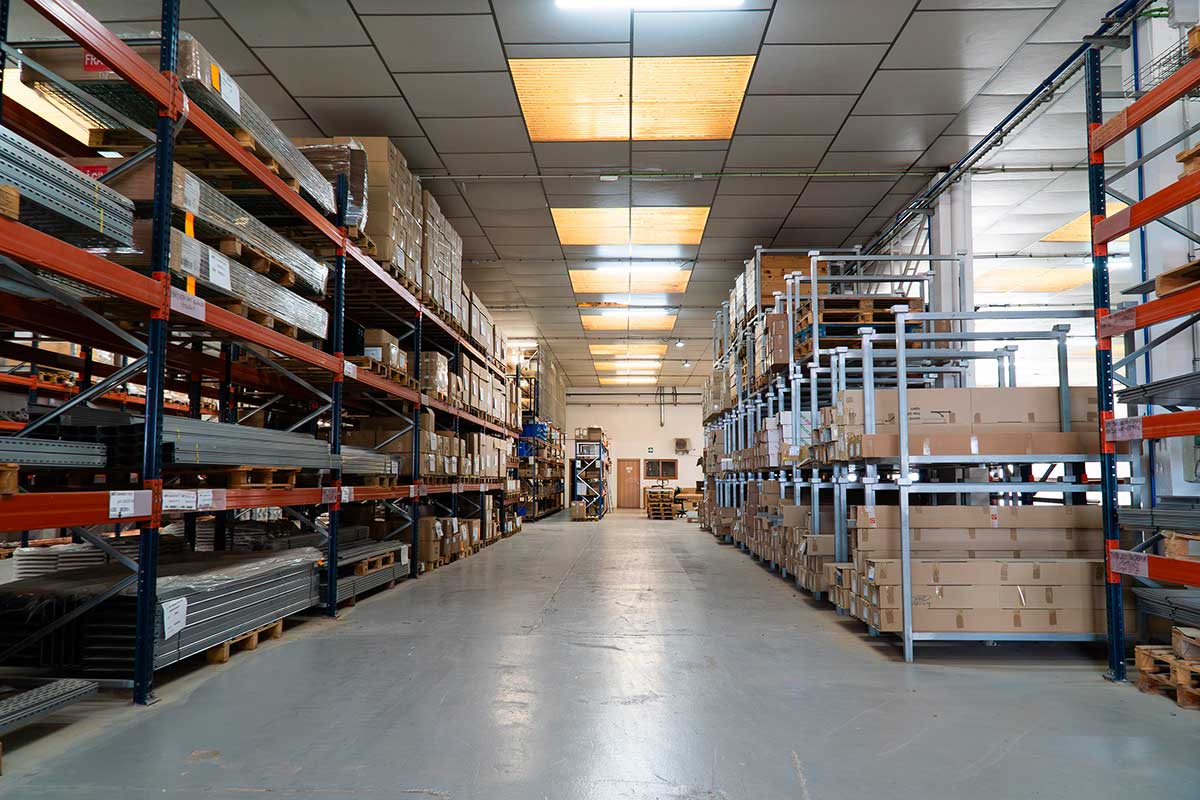 Pasillo amplio en un almacén con estanterías metálicas llenas de cajas y materiales apilados de forma ordenada.