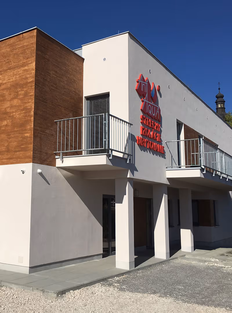 Moderná budova s balkónmi, obložená drevom a bielou omietkou pod jasnou modrou oblohou.