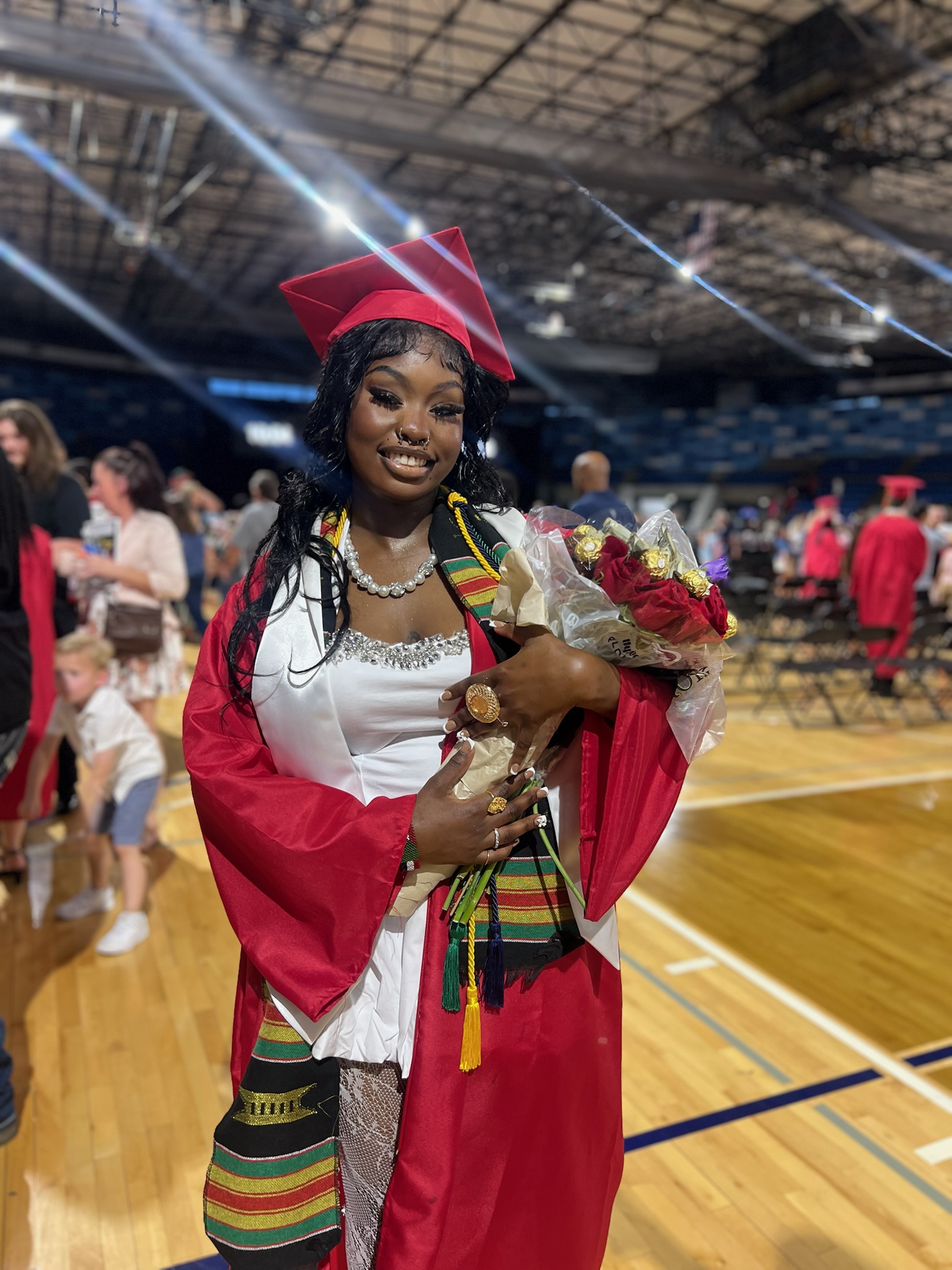 Photo of student at graduation wearing cap and gown, holding flowers