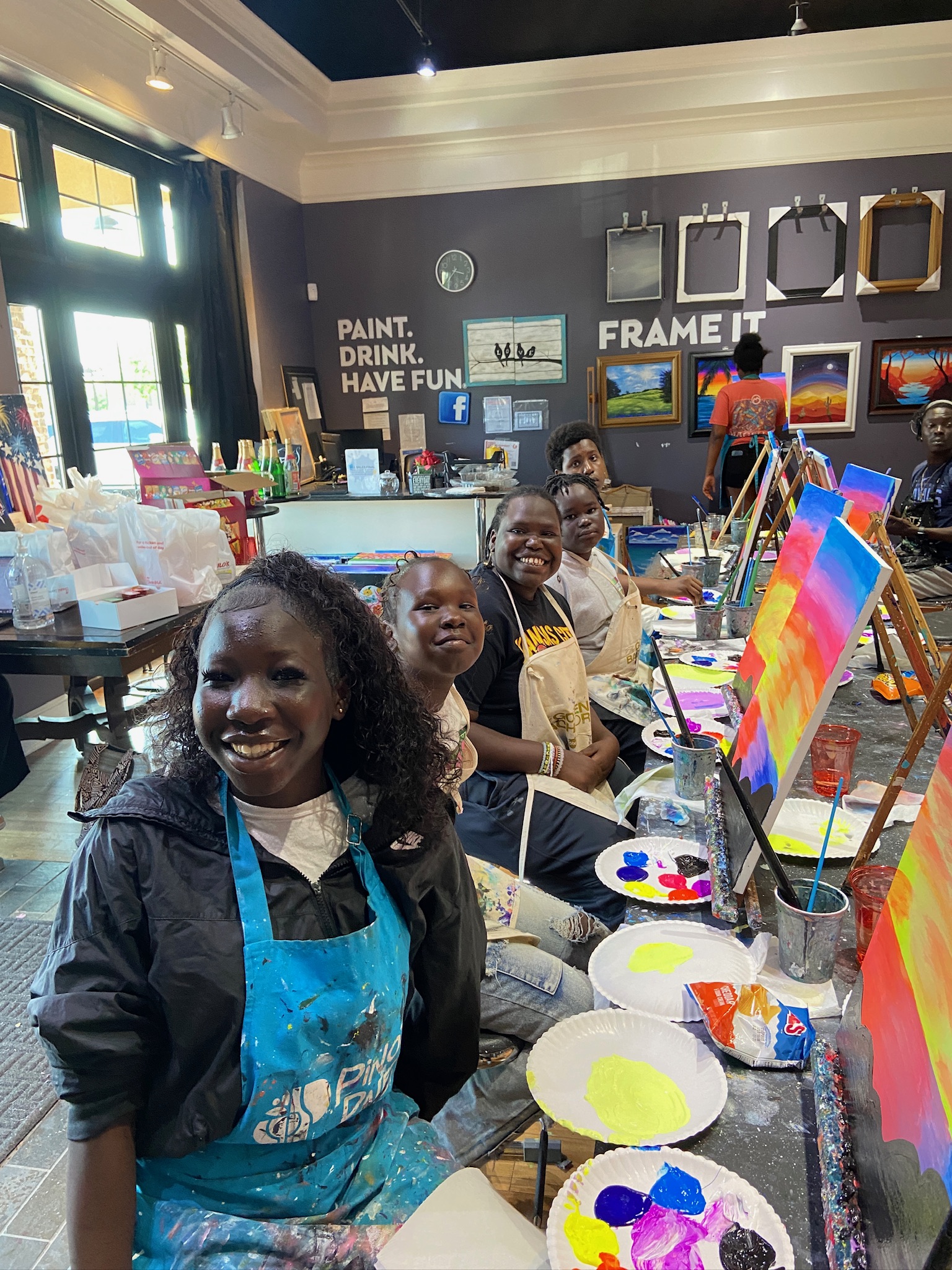 Photo of youth sitting in front of easel and paint, wearing painting aprons