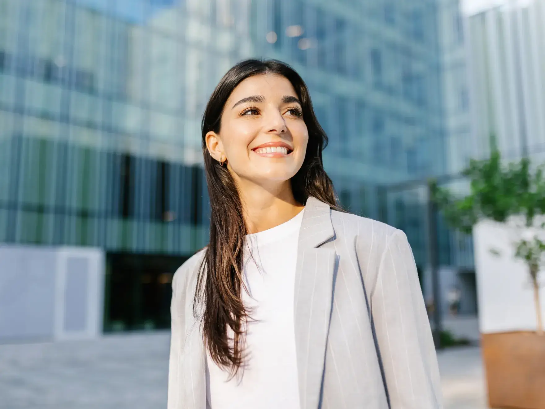 A person in a light blazer smiles while standing outside a modern glass building.