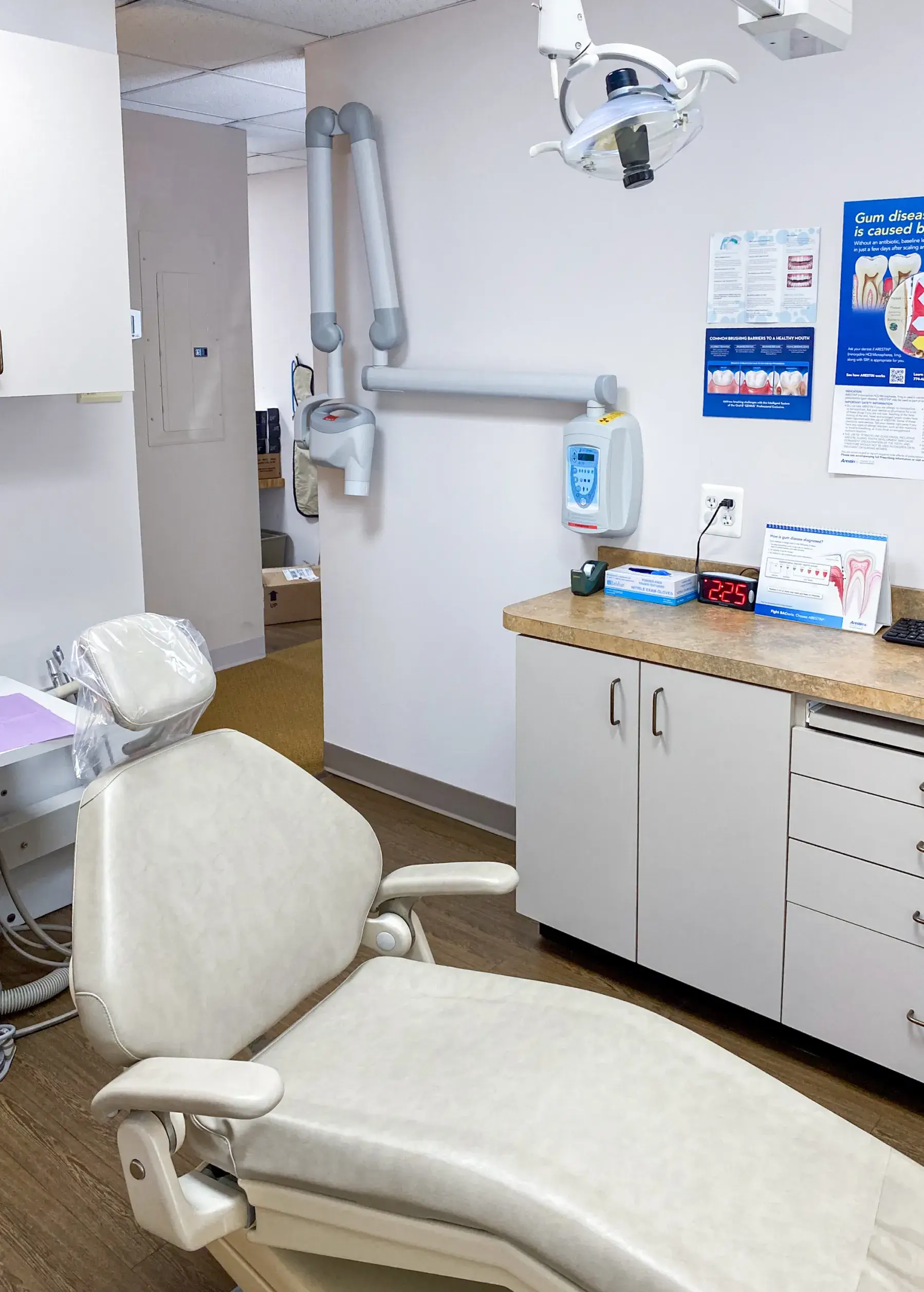A dental examination room with a reclined chair, overhead light, and wall-mounted dental equipment.