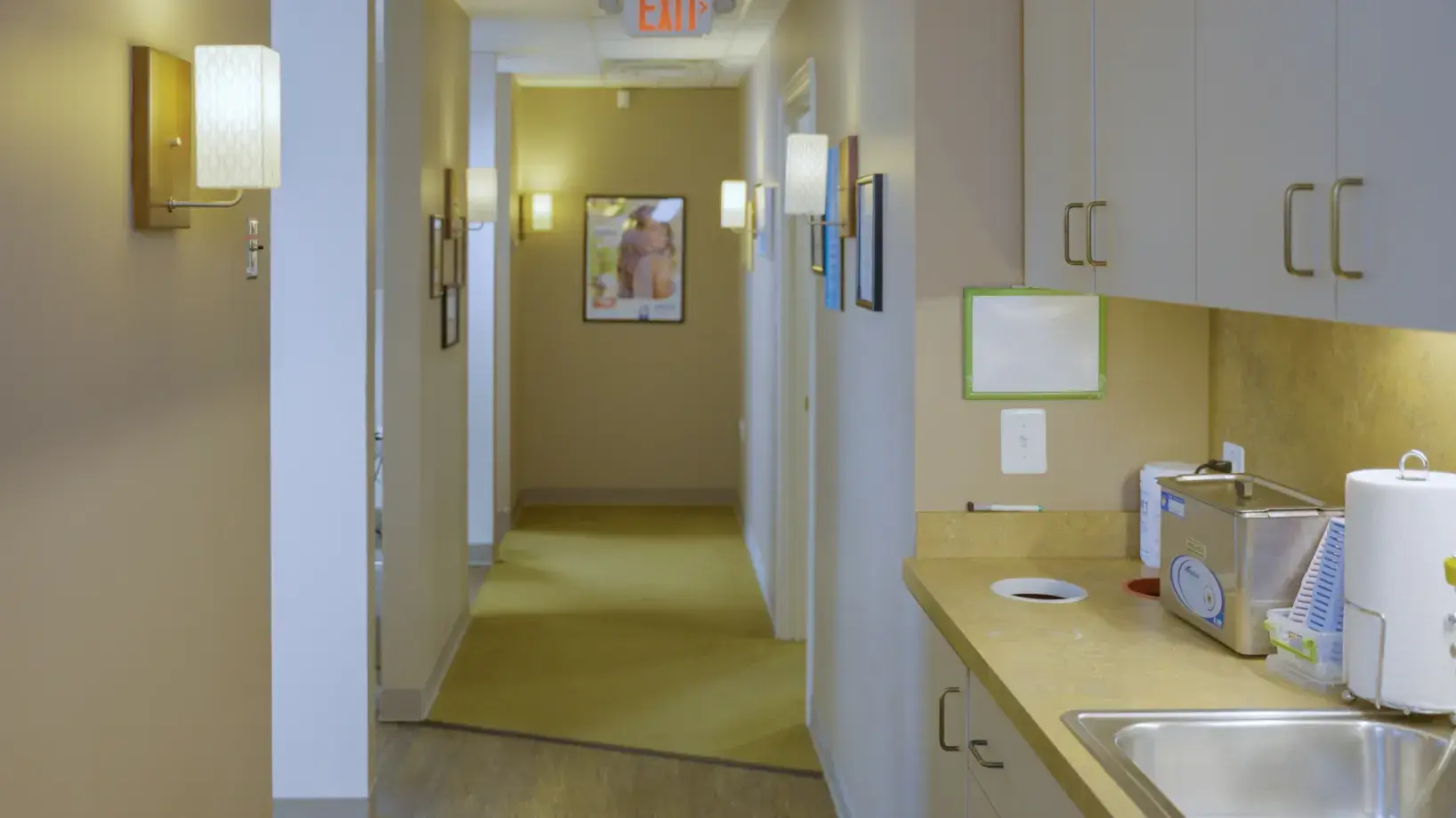 A narrow office hallway with a countertop, cabinets, and a sink on the right side.