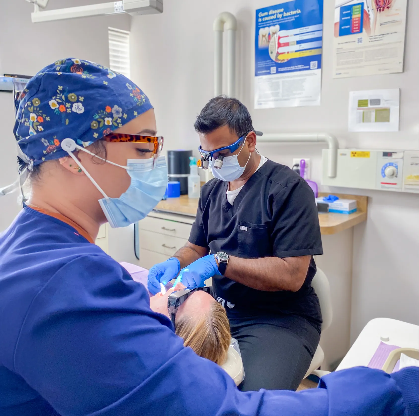 Dentists in masks and gloves perform a dental procedure on a patient in a clinic.