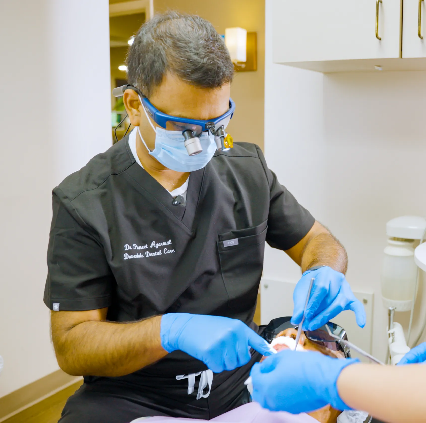 A dentist explains a procedure to a patient in a dental office, while an assistant observes.
