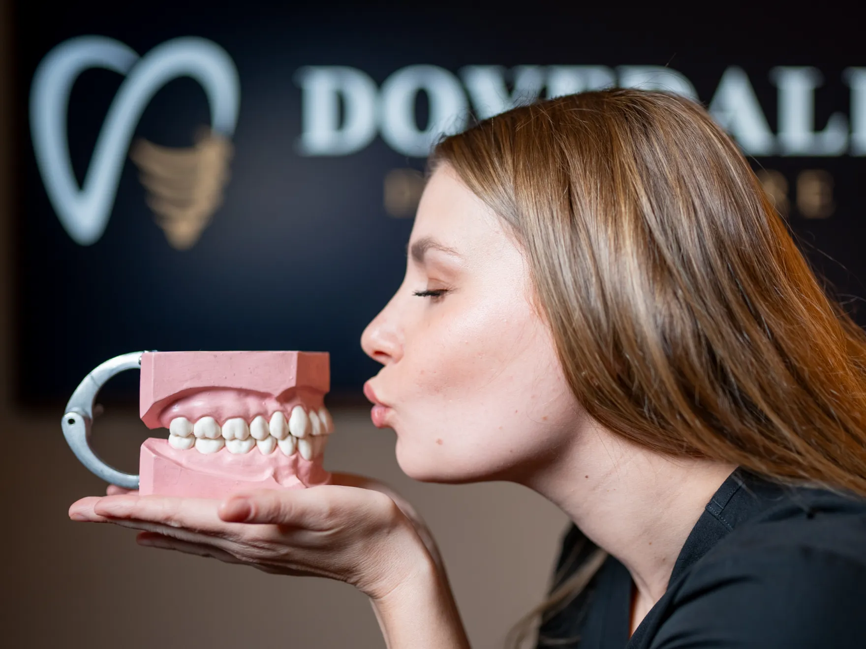 Two people in black medical scrubs smiling and walking in a hallway with a tablet.