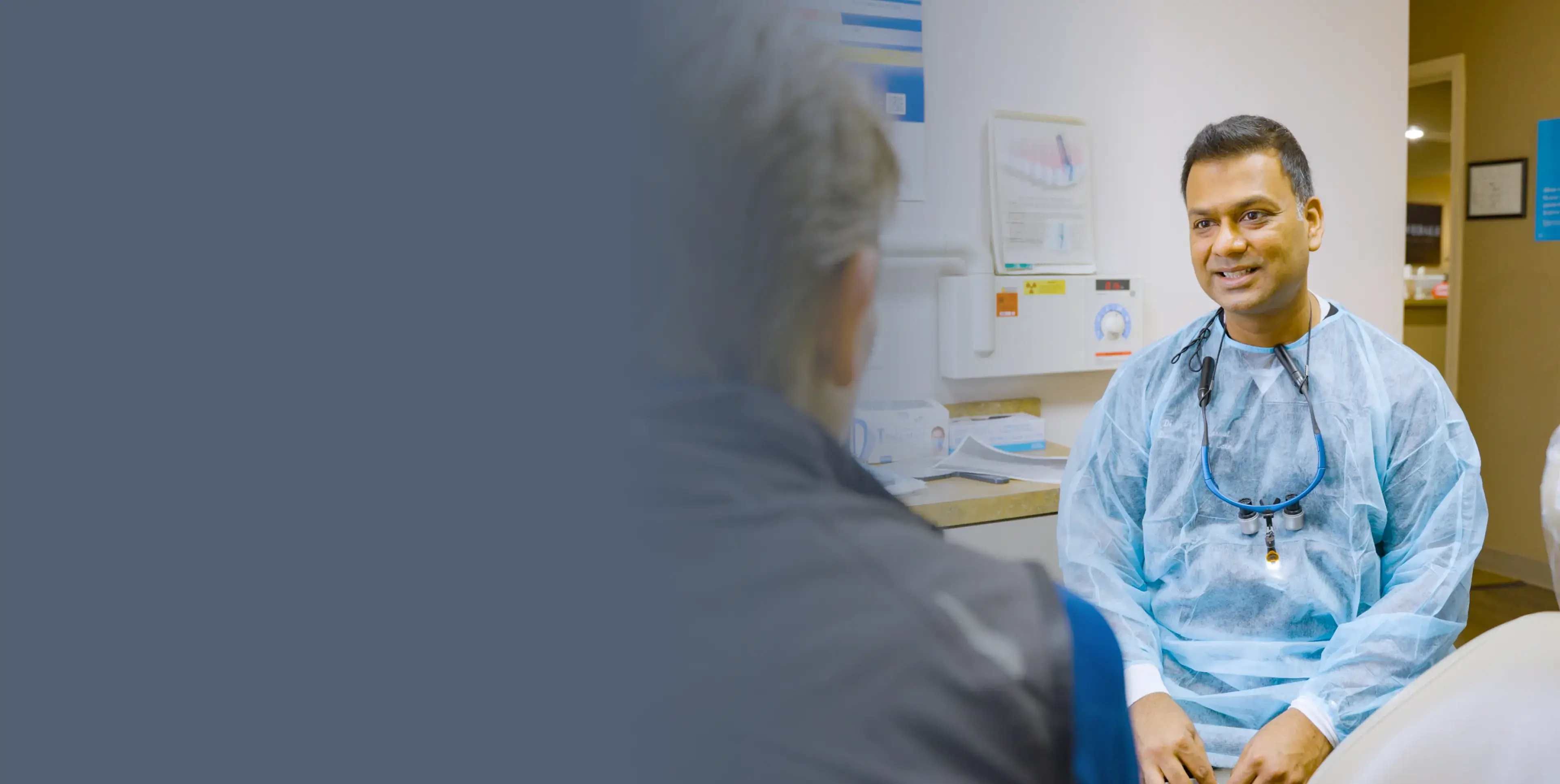 Medical professional talking to a patient in a hallway, holding a tablet and wearing a stethoscope.