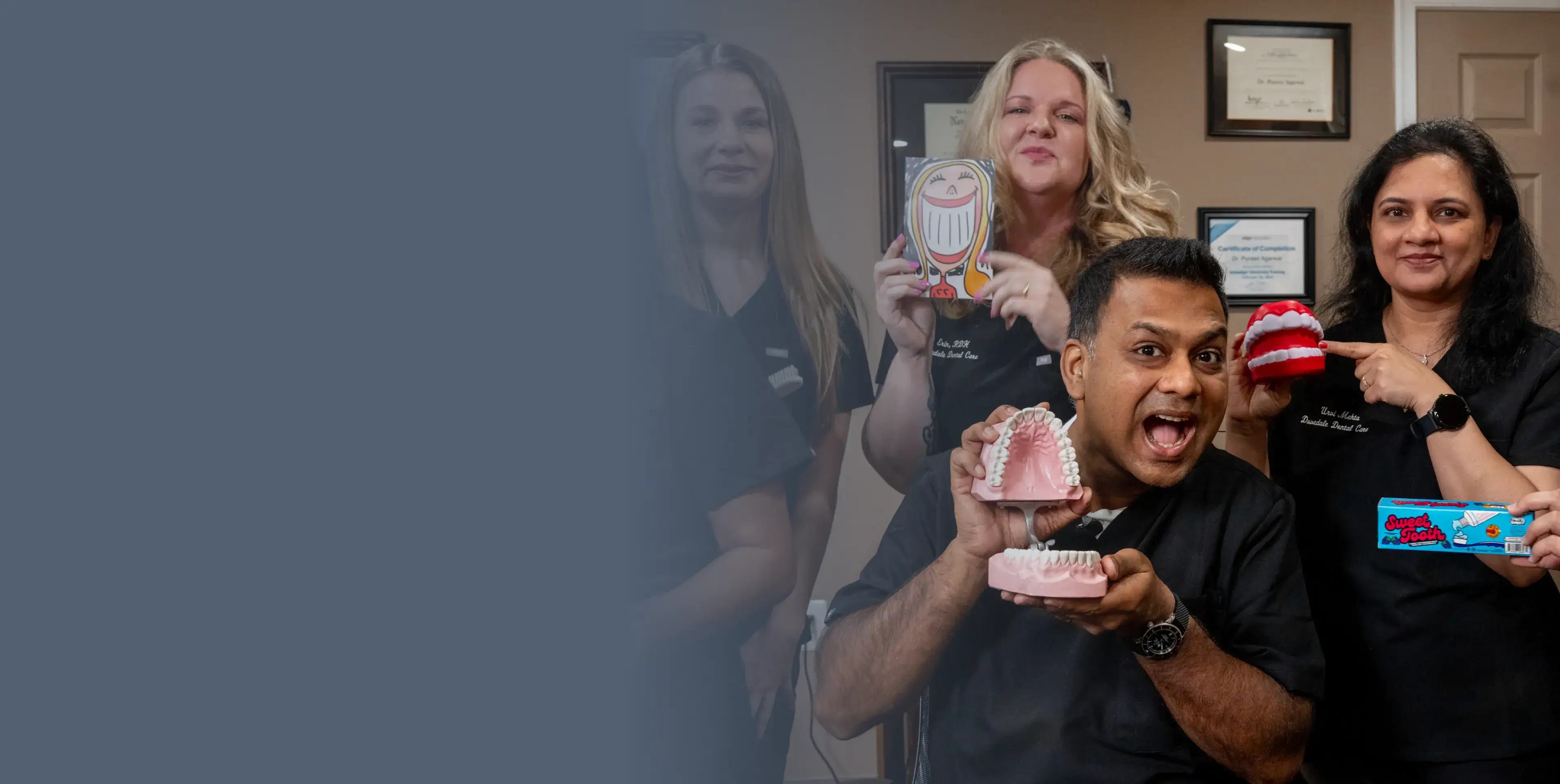 A dentist holds a model of teeth and playfully poses with smiling colleagues.