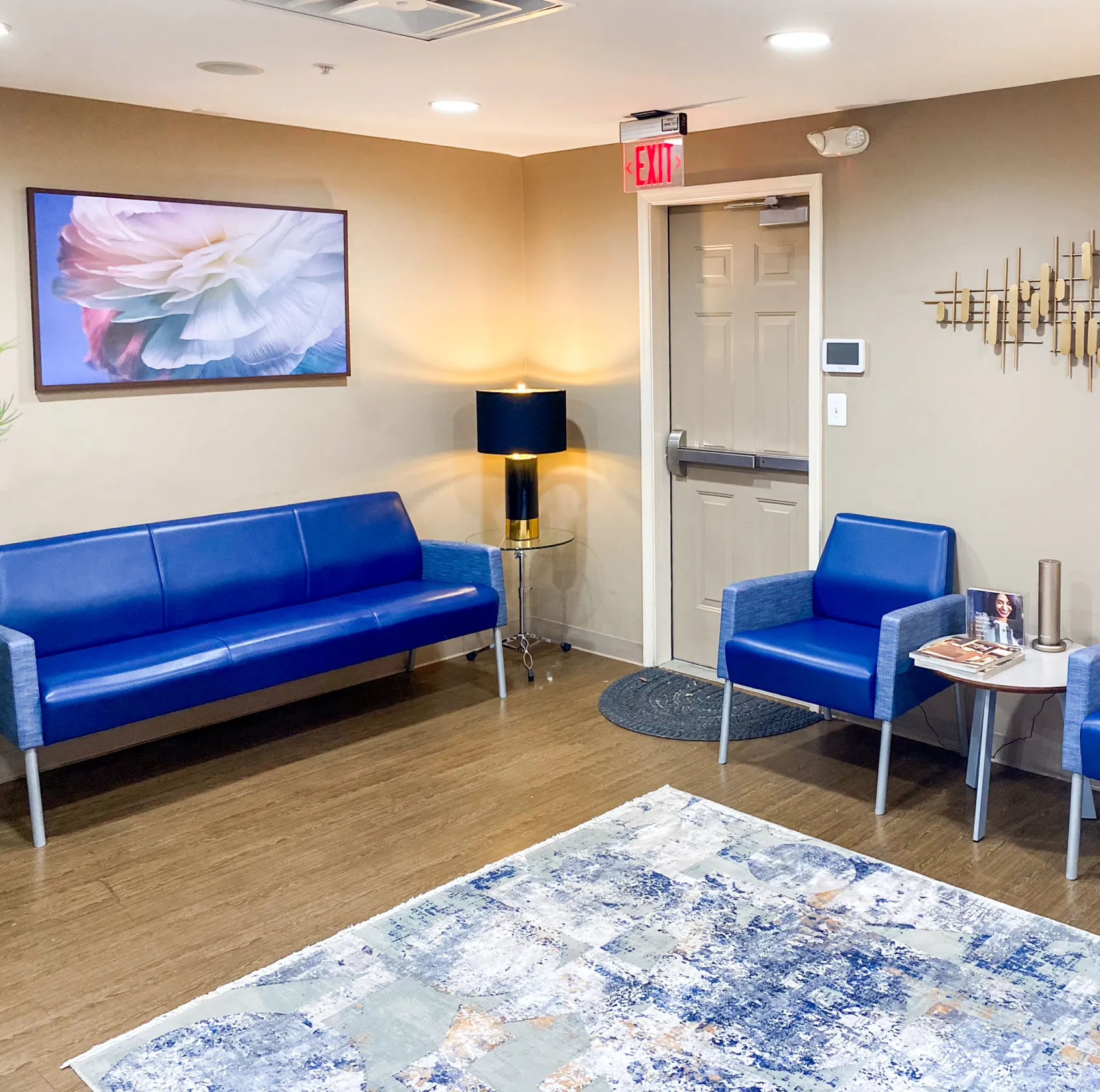 A waiting room with blue couches, a decorative rug, and framed wall art.