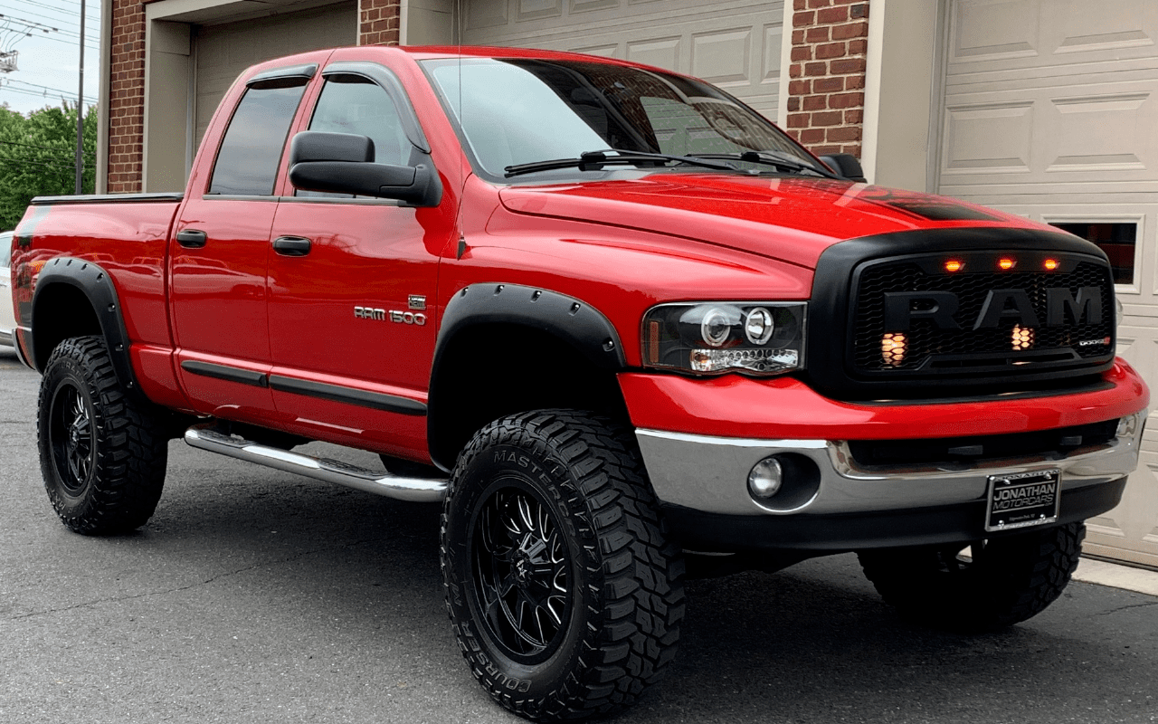 Camion Ram 1500 rouge avec grandes roues tout-terrain garé devant un garage résidentiel.