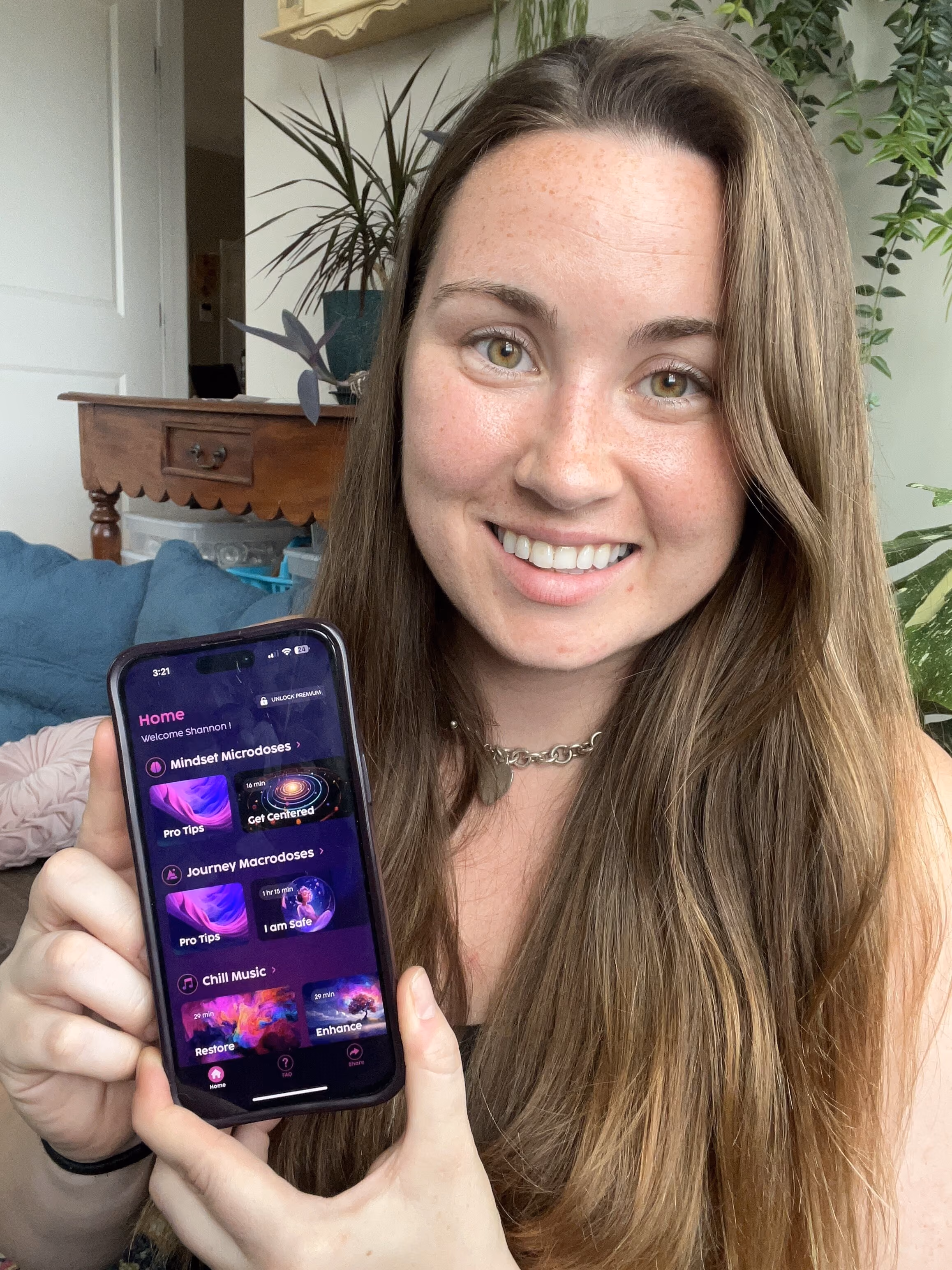 Smiling woman with long brown hair holding a smartphone displaying a Limitless mindset training, guided imagery meditation and music app interface.
