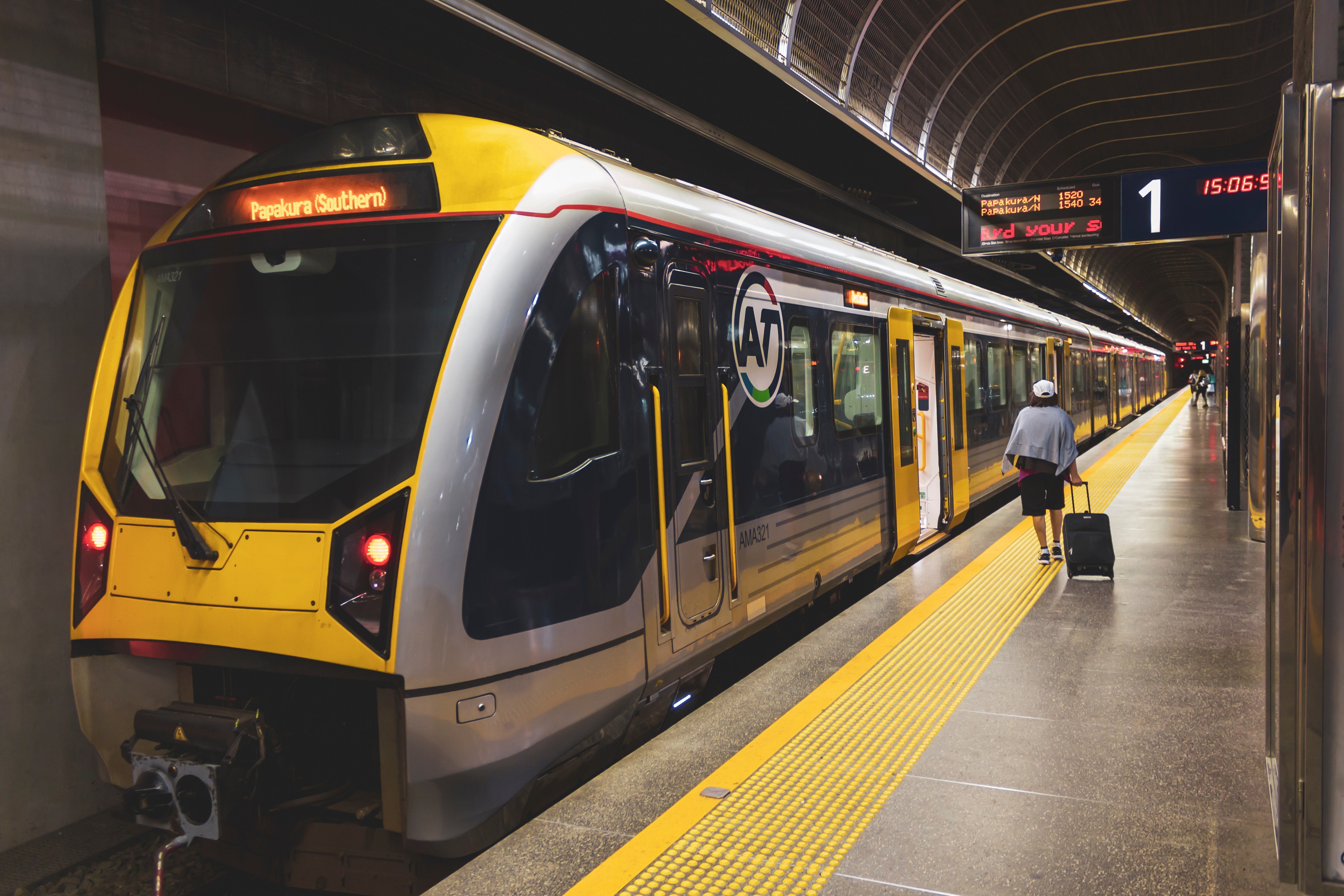 Modern yellow and black passenger train at a station platform with a person walking alongside carrying luggage.