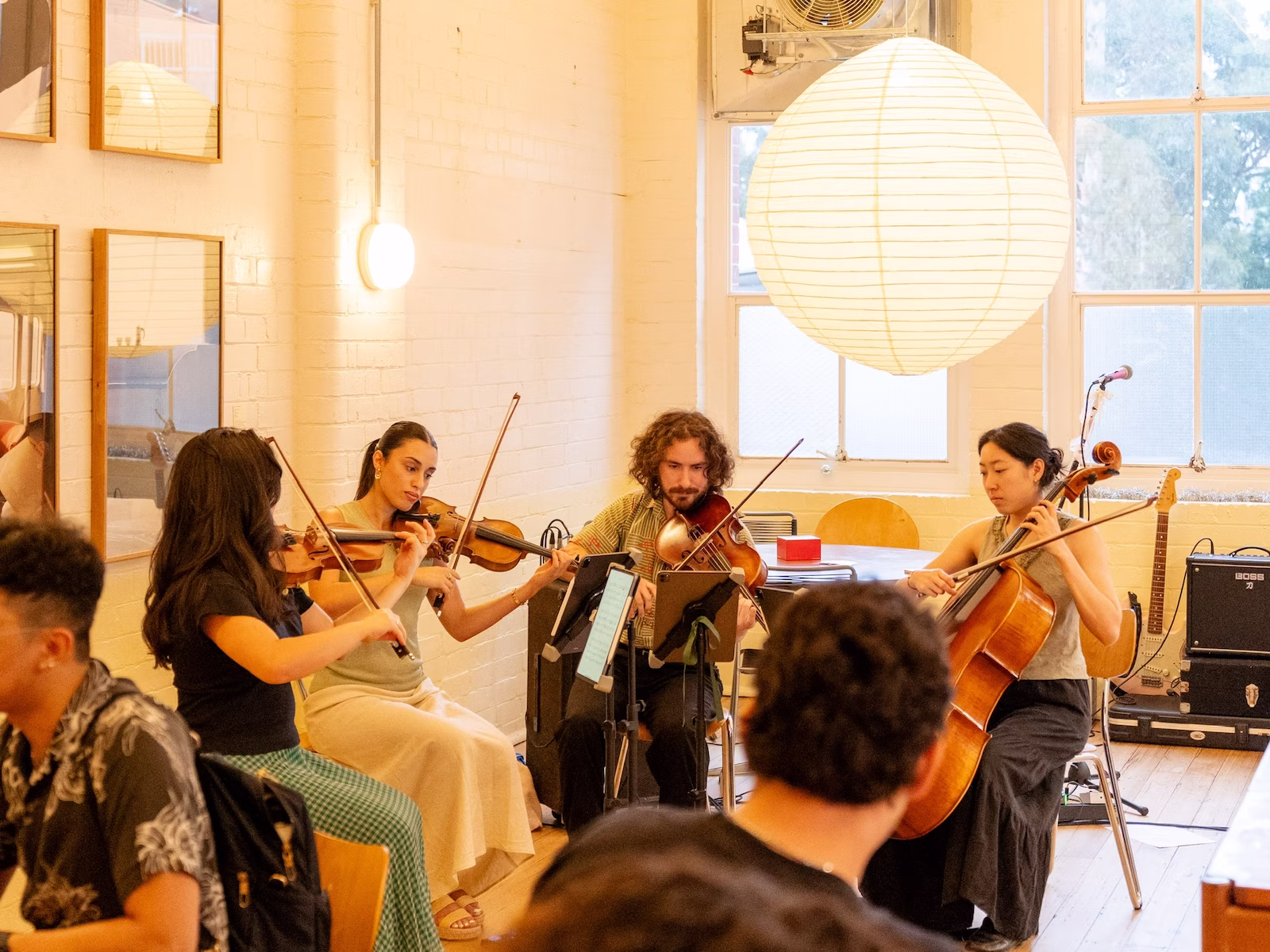 A string quartet performing in a cafe with a large paper light in background.