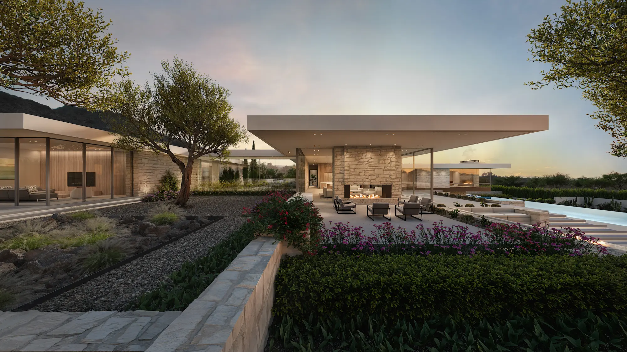 Modern outdoor patio with stone walls, seating around a fireplace, and landscaped garden at dusk.