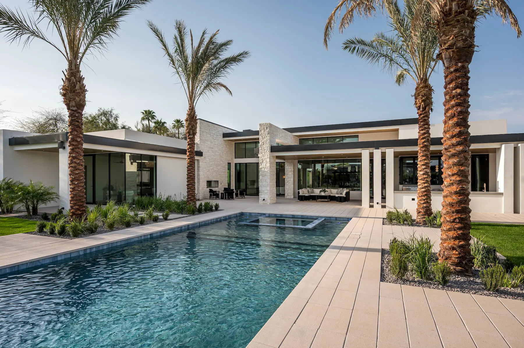 Modern house with large windows, palm trees, and a rectangular swimming pool in the foreground.