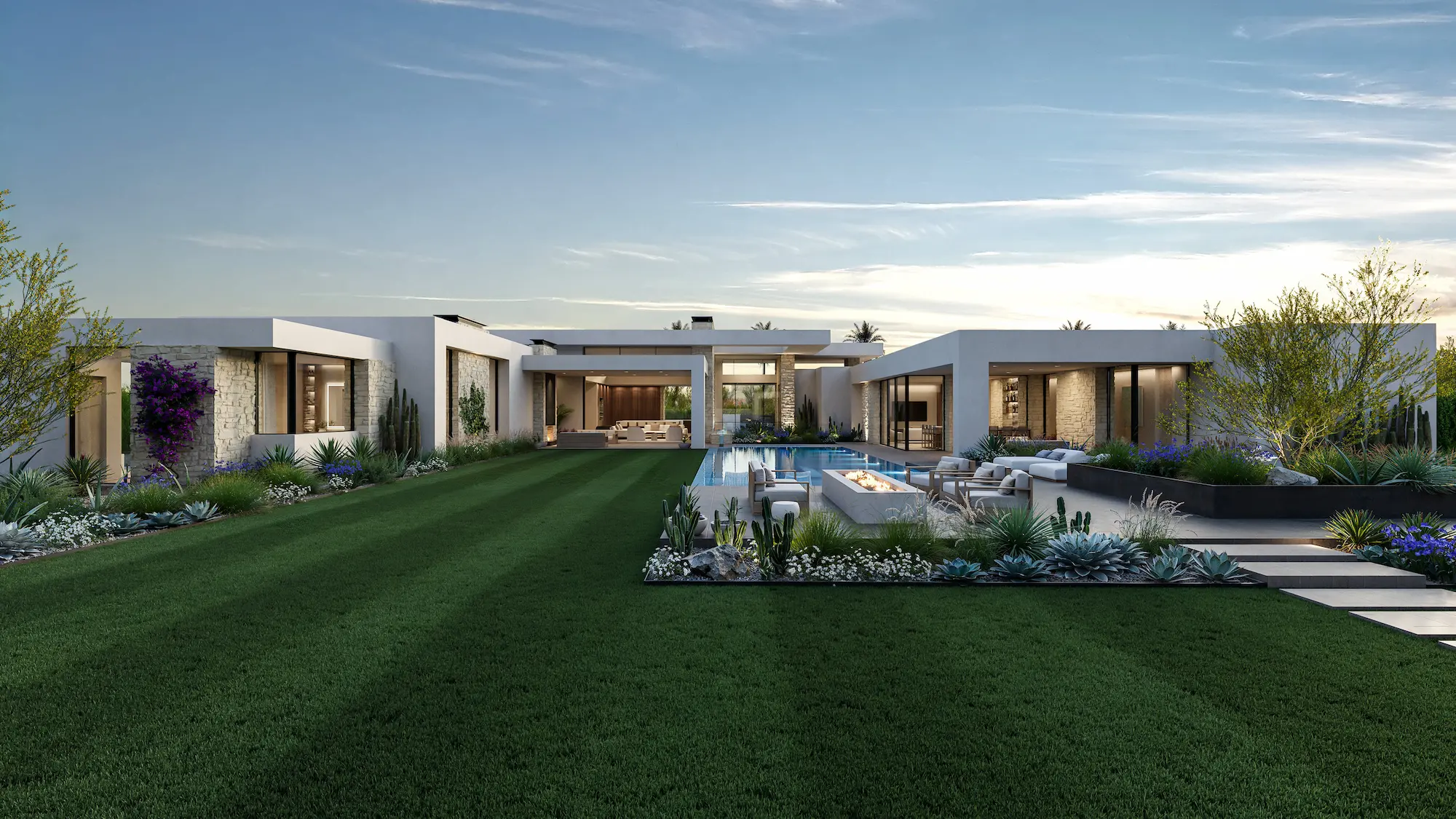 Modern luxury house with large glass windows, an infinity pool with water cascading over stone wall, lush landscaping, and mountain backdrop at dusk.