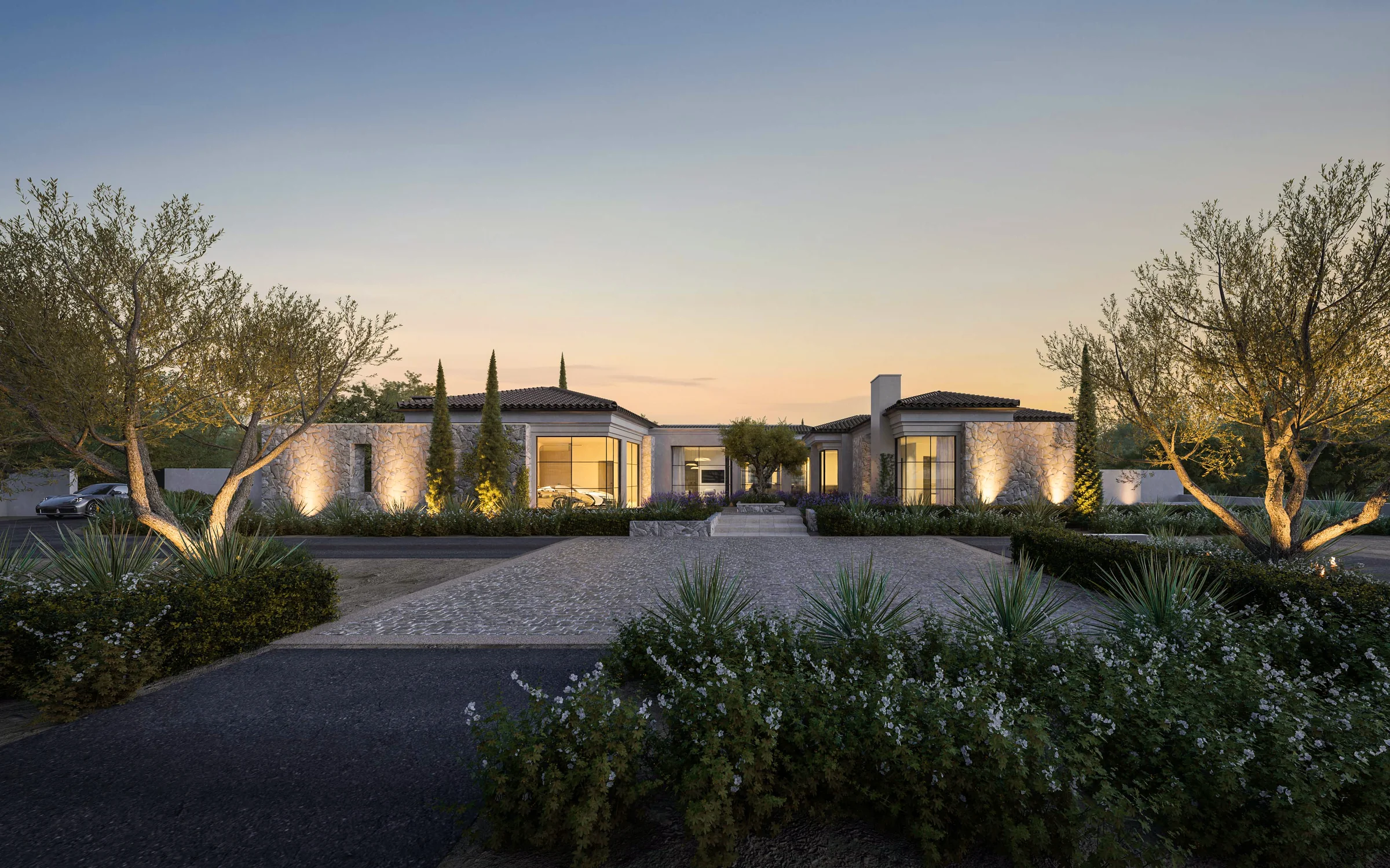 Modern luxury house with large glass windows, an infinity pool with water cascading over stone wall, lush landscaping, and mountain backdrop at dusk.
