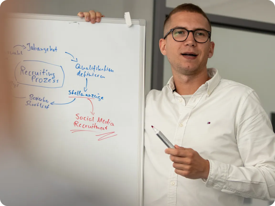 Ein Mann steht an einem Whiteboard, spricht dabei und hält einen Stift in der Hand.