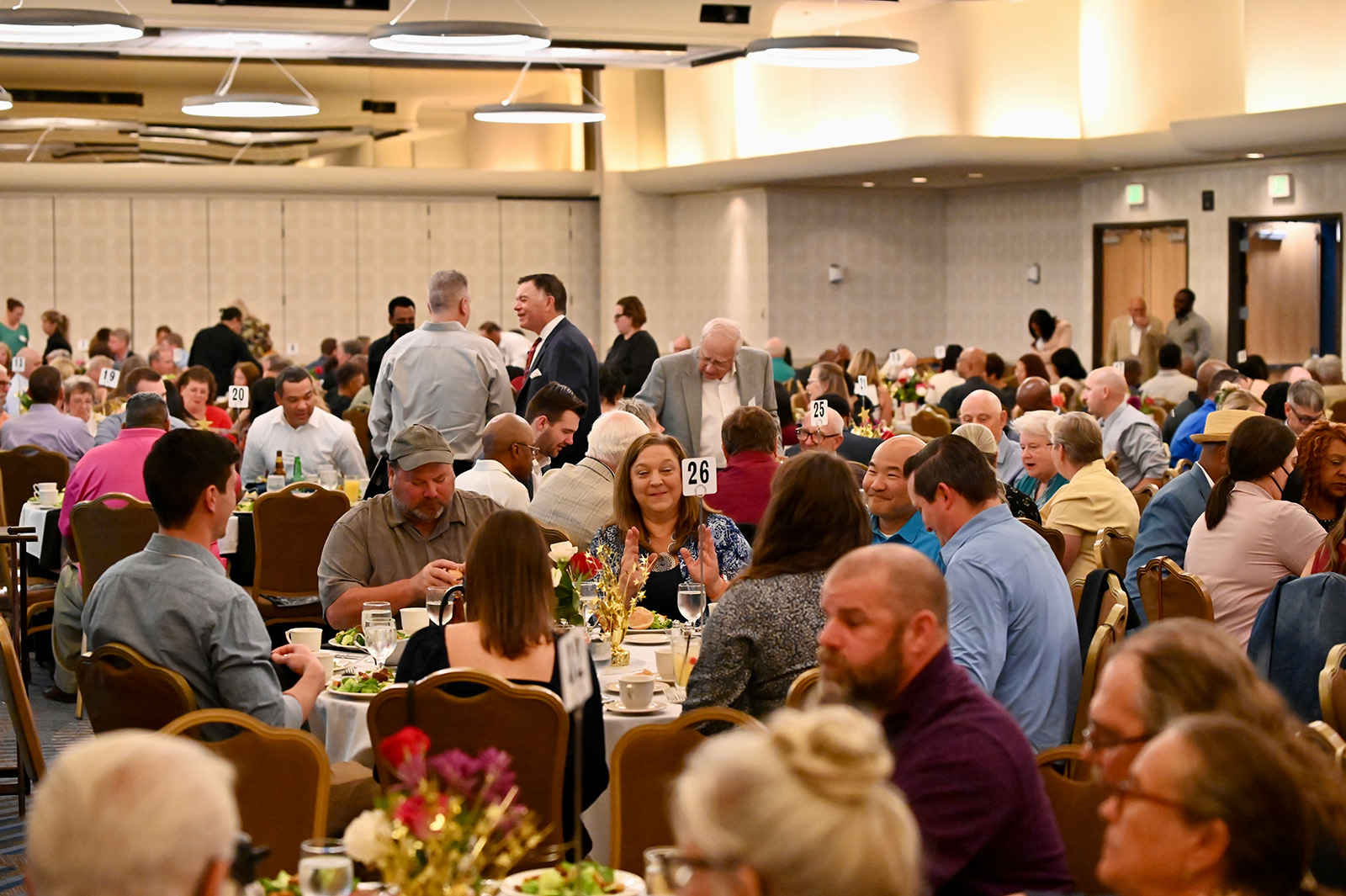 Large banquet hall filled with people seated at round tables enjoying a meal and conversation.