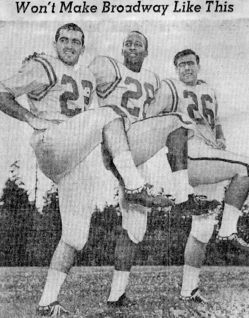 Three football players wearing jerseys numbered 23, 22, and 26 are standing outdoors, kicking their legs up in unison beneath the headline 'Won't Make Broadway Like This.'
