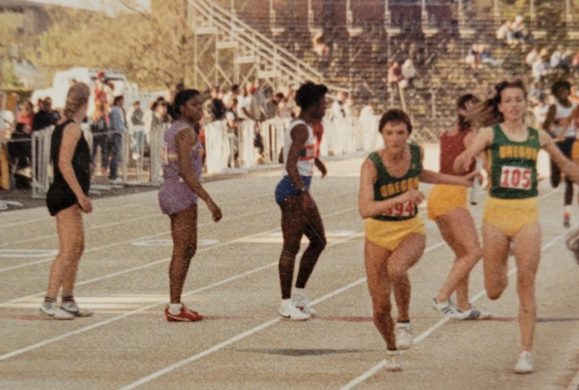 Track relay race baton handoff between two female runners in yellow and green Oregon uniforms.