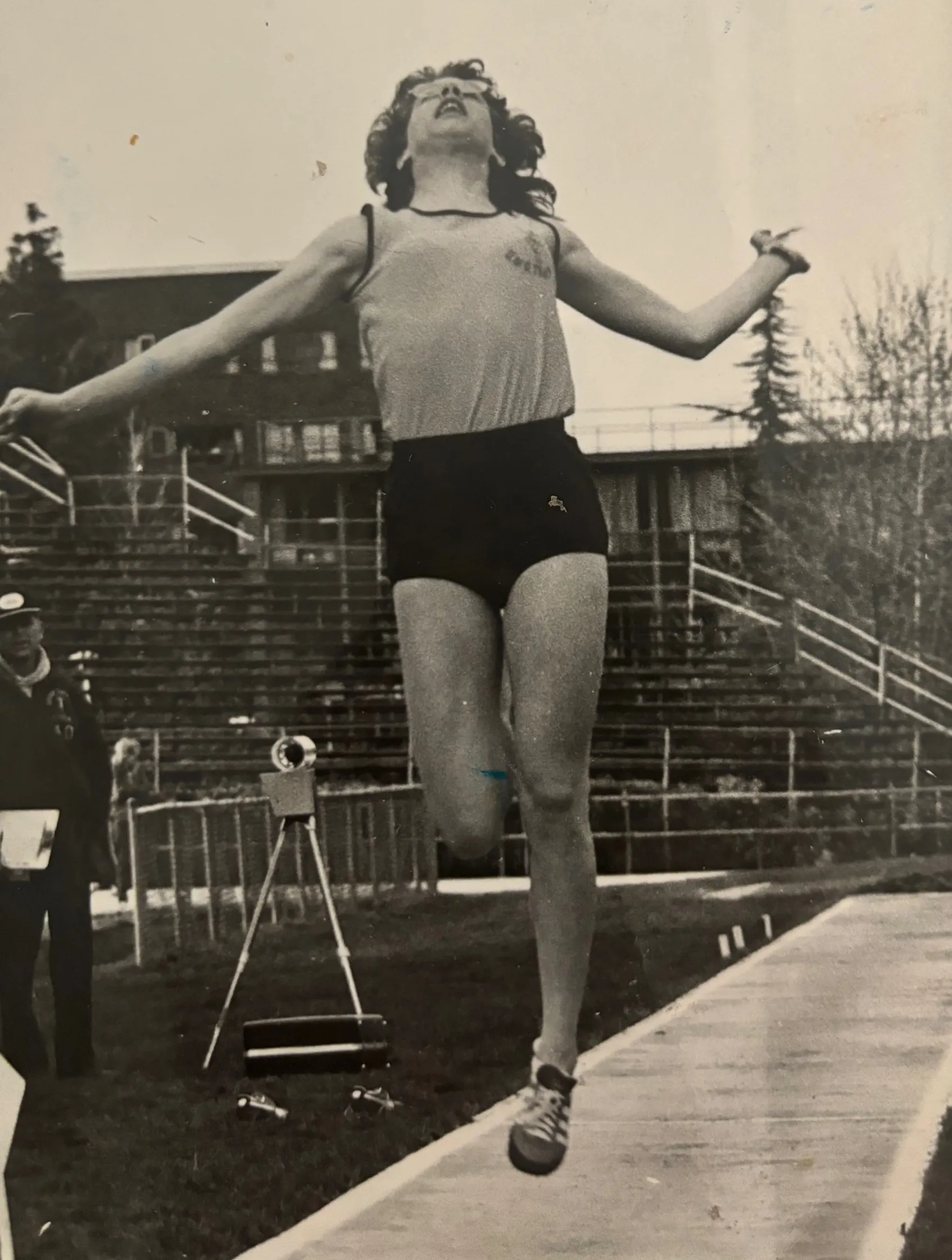 Young athlete in mid-air during a long jump at an outdoor track and field event with empty bleachers in the background.