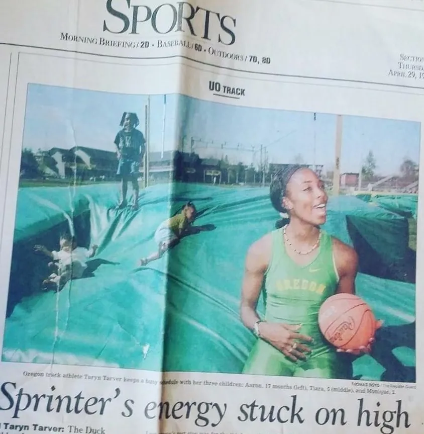Oregon track athlete Taryn Tarver in green athletic gear holds a basketball on a track covered with a tarp while her three young children play on the tarp behind her.