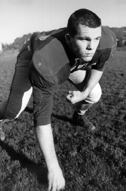 Black-and-white photo of a football player in full gear crouching on the field, ready to start a play.