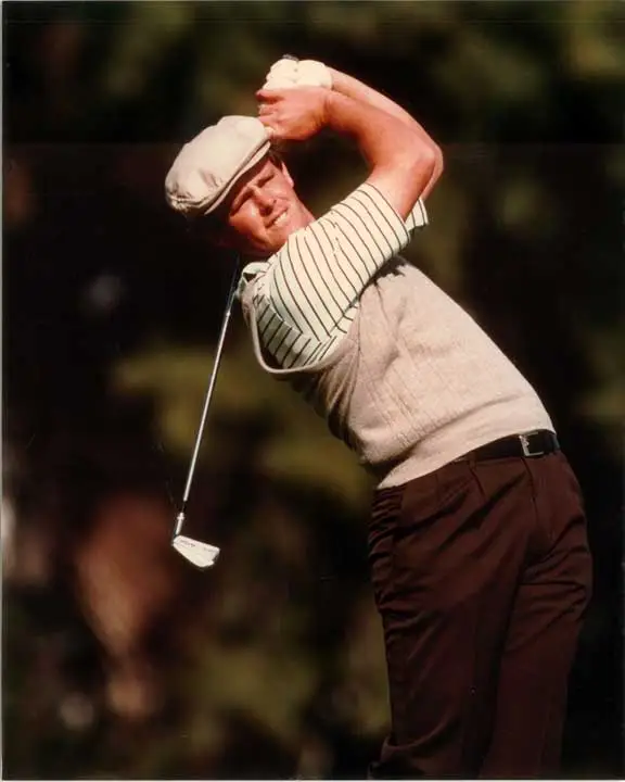 Golfer in vintage attire mid-swing, wearing a flat cap, striped shirt, and sweater vest.