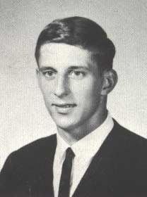 Black and white portrait of a young man wearing a dark suit, white shirt, and tie, posing for a formal photo.