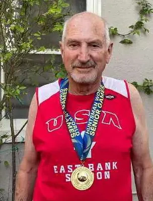 Elderly man wearing a red USA sleeveless shirt and a gold medal on a blue ribbon around his neck.