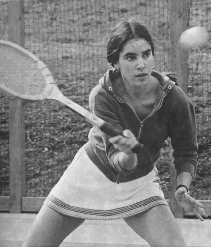 Young woman in a skirt and hoodie preparing to hit a tennis ball with a racket on an outdoor court.
