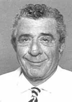 Black and white portrait of a smiling man with curly hair wearing a white shirt and striped tie.