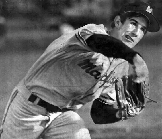 Black and white photo of a baseball player in a uniform throwing a ball with a glove on his left hand.