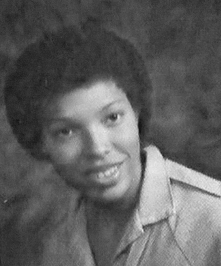 Black and white portrait of a young woman with short curly hair wearing a collared shirt, smiling slightly.