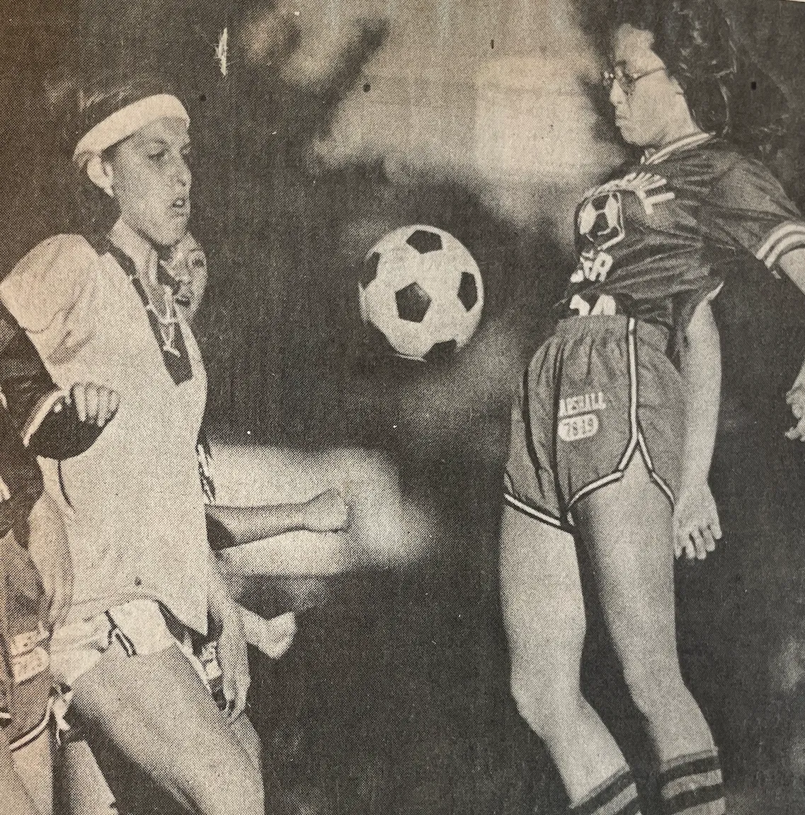 Two female soccer players competing for a black-and-white soccer ball midair during a match.
