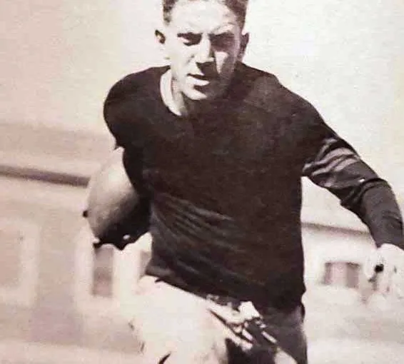 Black and white photo of a young man running with a football under his right arm during a game.