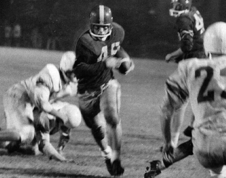 Black-and-white photo of a football player wearing number 45 running with the ball while other players attempt to tackle him.