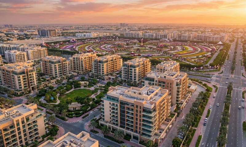 Aerial view of Arjan Dubai showing modern apartments, green spaces, and Dubai Miracle Garden background