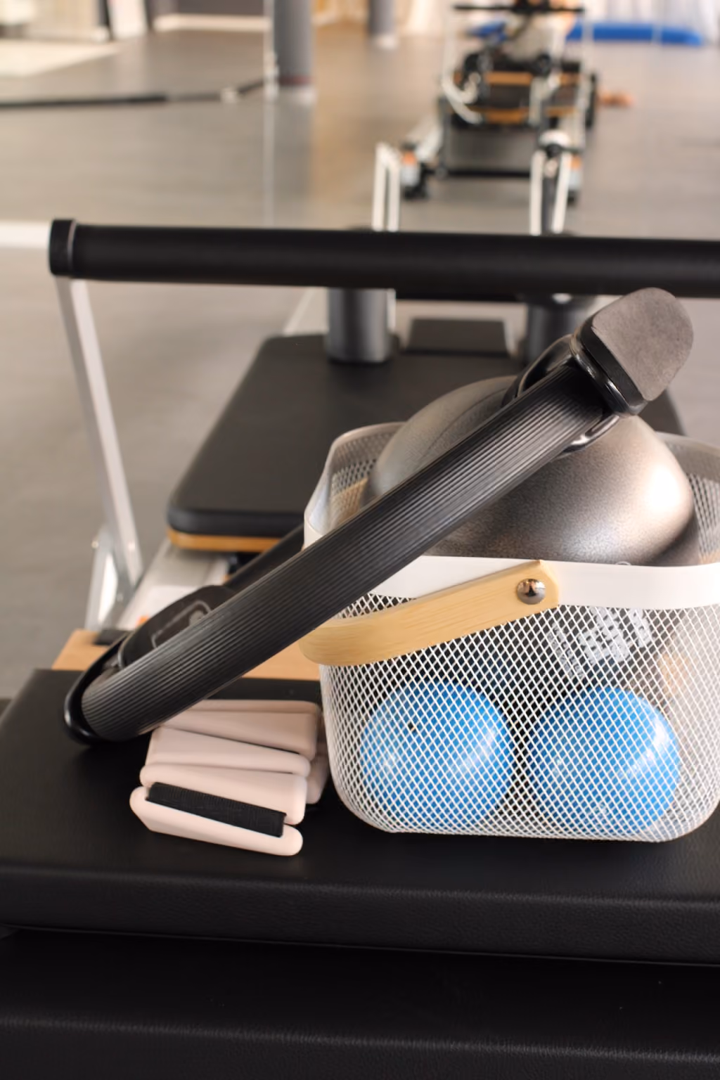 Ein Netzkorb mit Fitnessbällen und -geräten an einem Pilates-Reformer-Gerät in einem Fitnessstudio.
