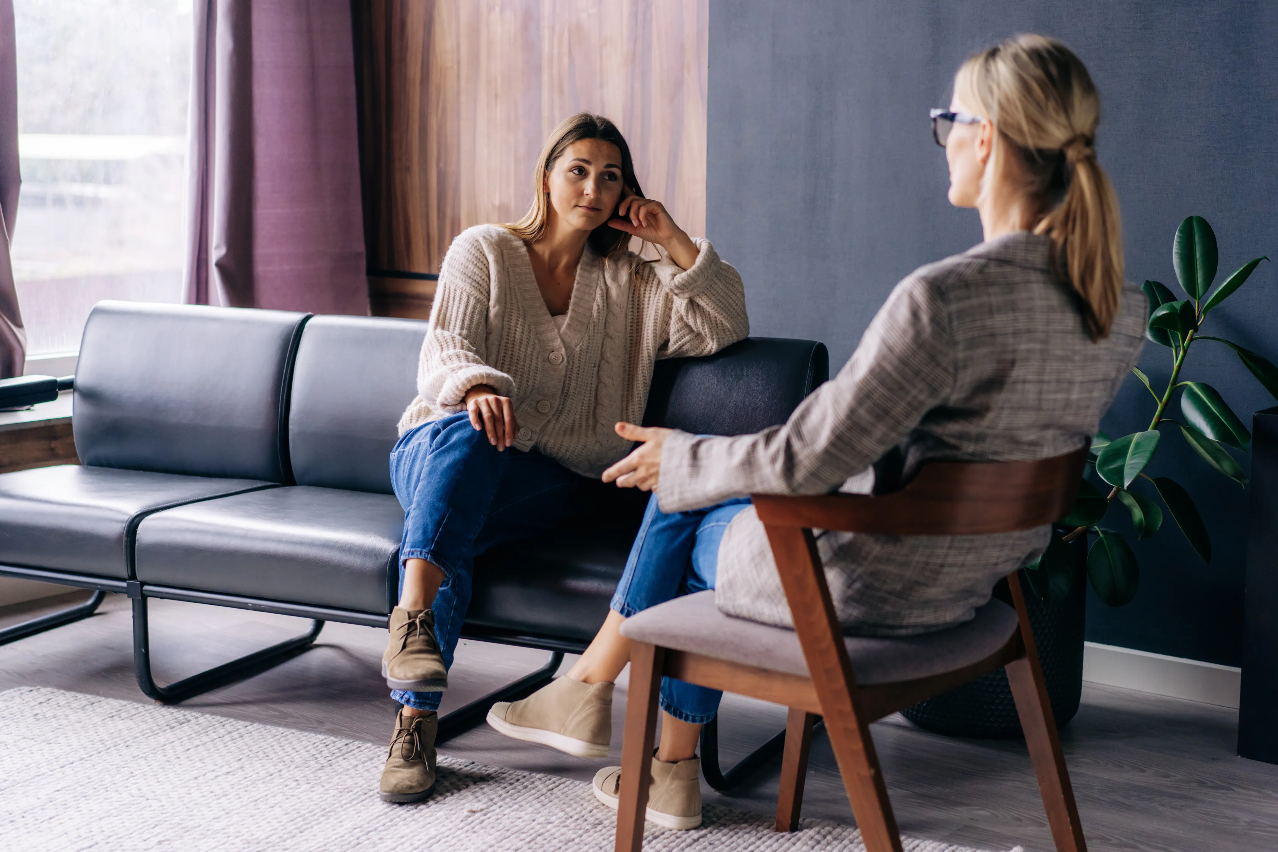 Une femme assise sur un canapé qui parle à une autre femme assise sur un fauteuil