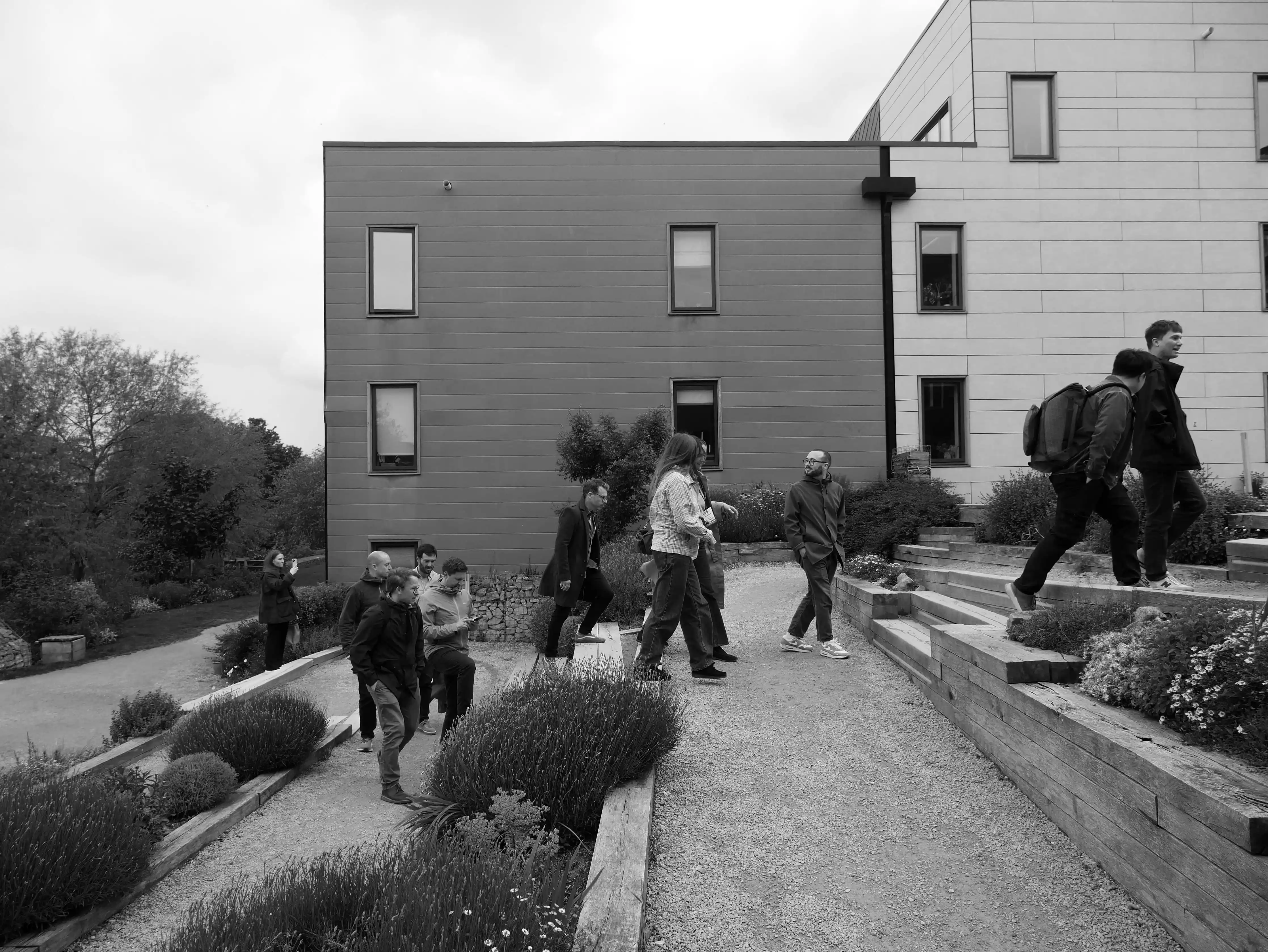 Group of people riding bicycles on a paved pathway between green lawns and tall modern brick buildings.