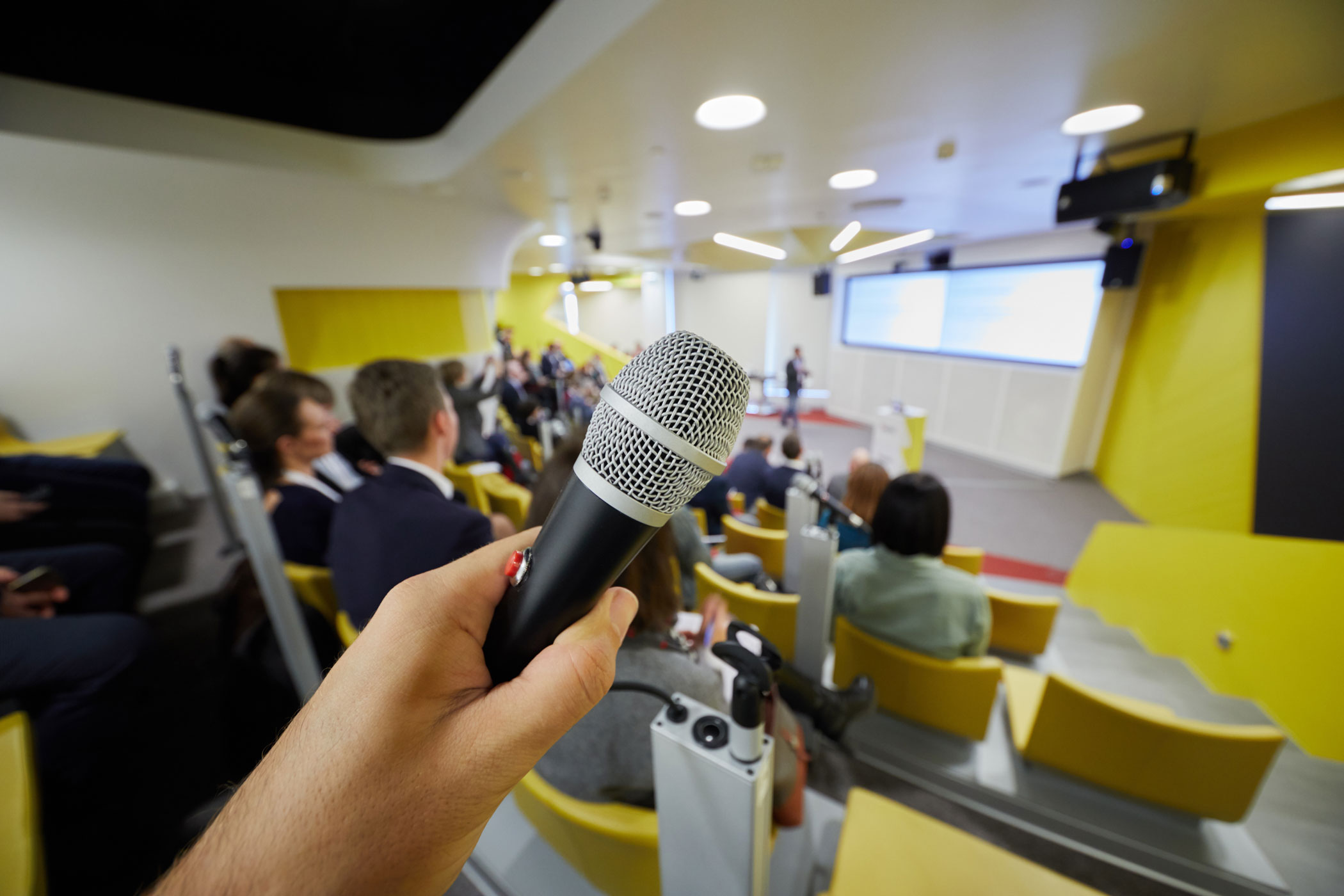 An image of a hand holding a microphone at a an auditorium where a product launch or press event is being hosted