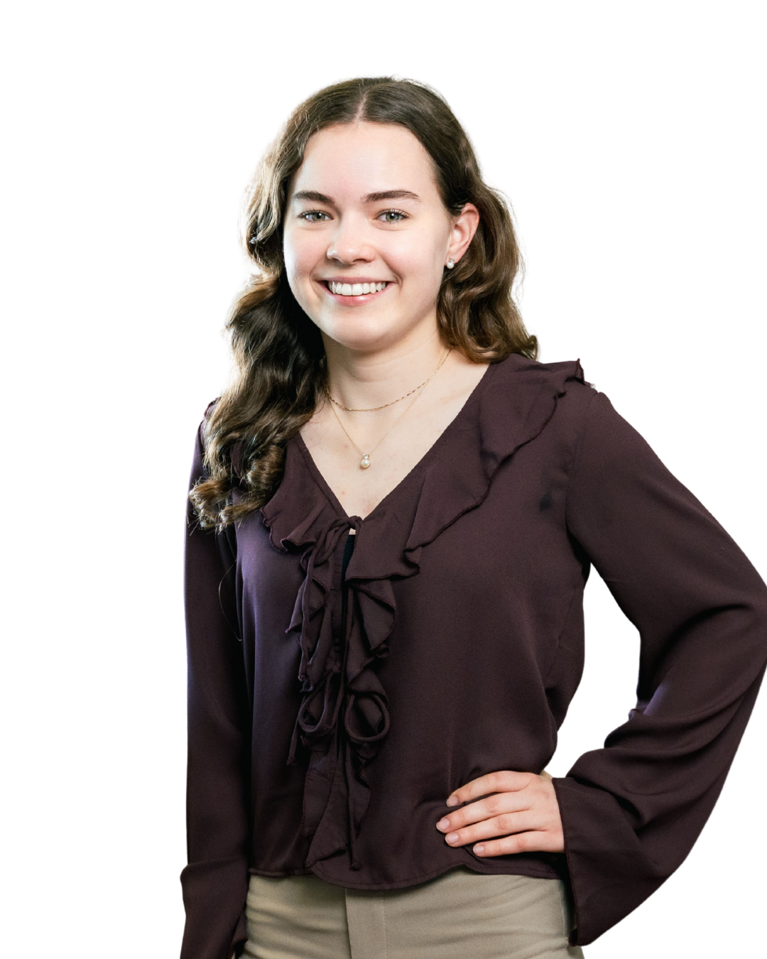 Smiling woman with curly brown hair, wearing a dark purple blouse and beige pants, hand on hip.