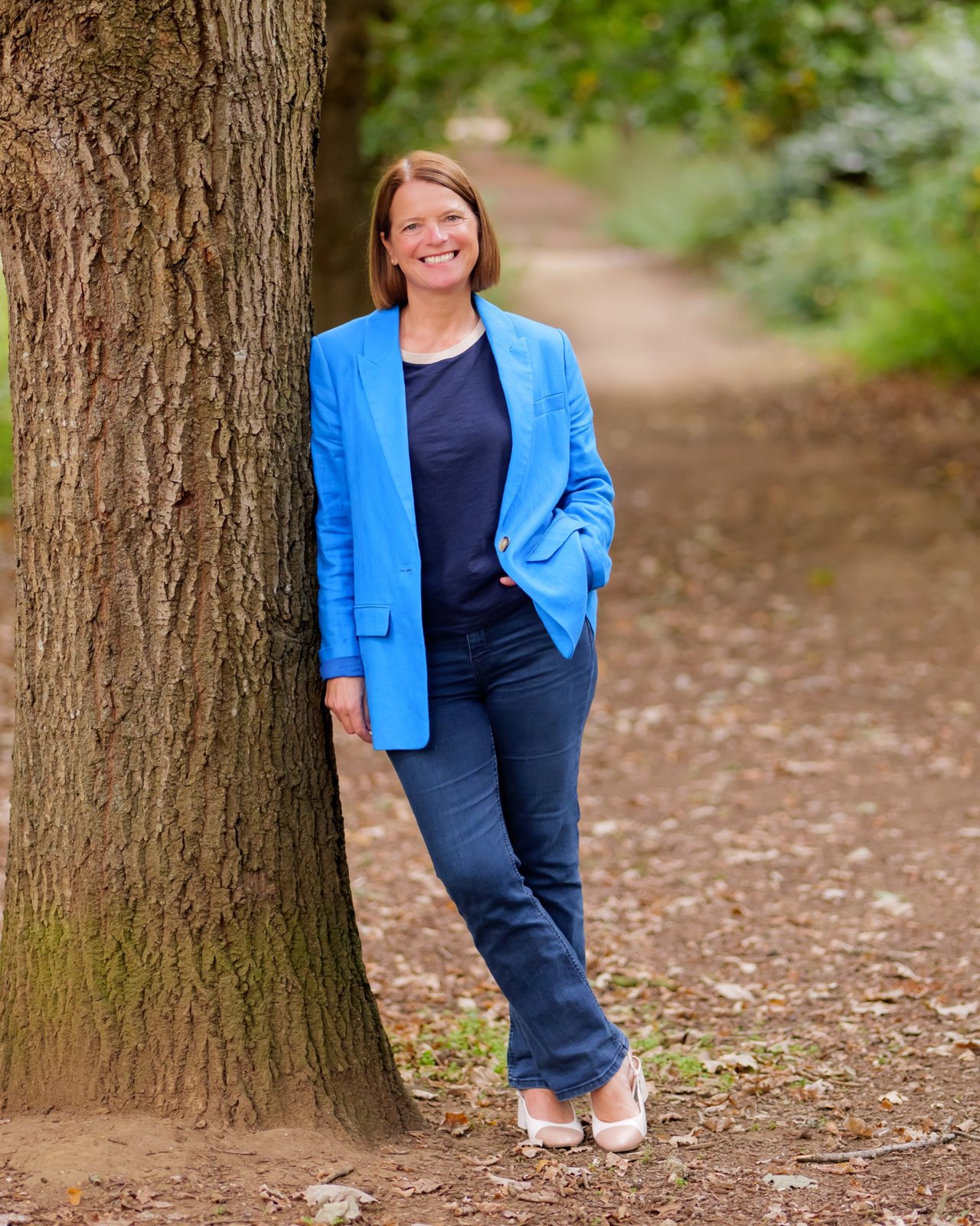 Niki Corbishley, leadership coach and author, leaning against a tree